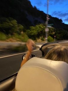 two people in a convertible driving down the road at night with mountains in the background