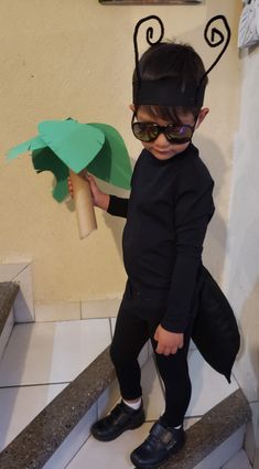 a young boy wearing sunglasses and holding a paper tree on the steps in front of him