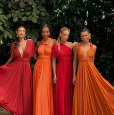 four women in orange and red dresses standing next to each other with trees behind them