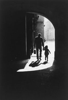 a black and white photo of a man holding the hand of a small child as they walk through an archway