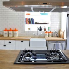 a stove top oven sitting inside of a kitchen next to a wooden counter and white cabinets