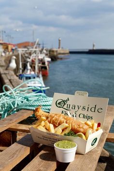 a fish and chips box sitting on top of a wooden table next to the water