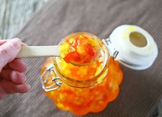 a person holding a spoon over a jar filled with jelly