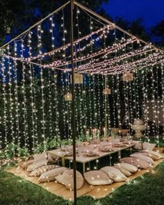 an outdoor dining area with string lights and pillows on the ground in front of it