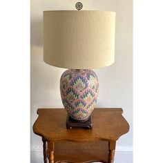 a table lamp sitting on top of a wooden table next to a white wall with a clock above it