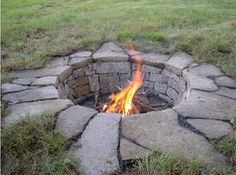 an open fire pit in the middle of a field with grass and rocks around it