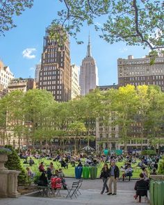 many people are sitting in the park near tall buildings