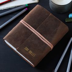 a brown leather journal sitting on top of a table next to pencils and markers