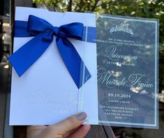 a person holding up a wedding card with a blue bow on the front and back