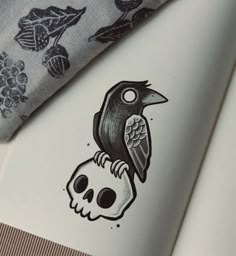 a black bird sitting on top of a skull next to a flowered cloth with skulls