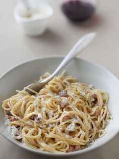 a white bowl filled with pasta and meat on top of a table next to a fork