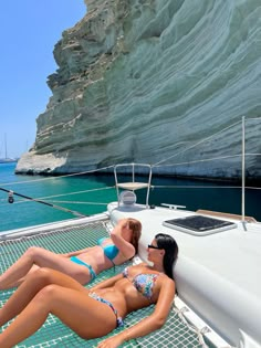 two women in bikinis laying on the deck of a boat