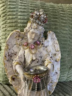 an angel figurine sitting on top of a pillow next to a bowl with jewels in it