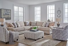 a living room with couches, chairs and ottomans in front of two large windows