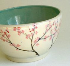 a white bowl with pink flowers painted on the side and green rim, sitting on a table