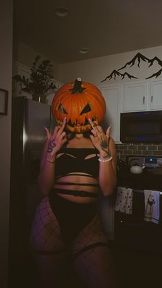 a woman in fishnet stockings holding a pumpkin over her head while standing in a kitchen