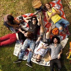 a group of people laying on top of a blanket in the grass next to each other