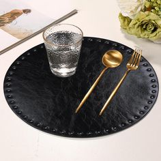 a black plate with a gold spoon and fork next to a glass on the table