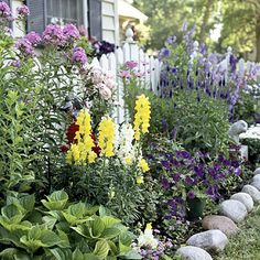 a garden filled with lots of flowers next to a white picket fence