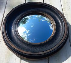 a round mirror on the side of a wooden deck with trees reflected in it's reflection