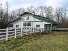 a white barn with a green roof and fence