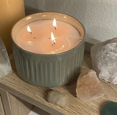 three lit candles sitting on top of a wooden table next to rocks and crystal stones