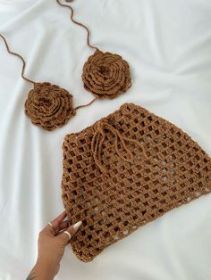 a crocheted purse and matching earrings on a white sheet with a person's hand