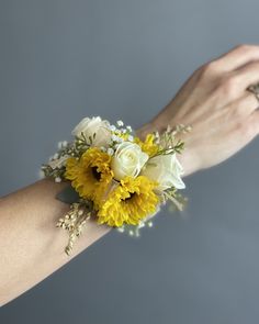 a woman's arm holding a yellow and white wrist corsage with flowers