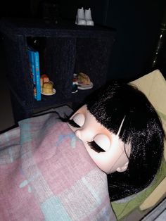 a doll is laying in bed with food on the table next to it and she has her eyes closed