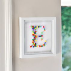 the letter e is made out of candy beads and framed in a white shadow box