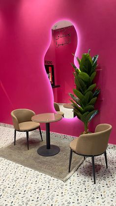 a pink room with two chairs and a round table in front of a large mirror