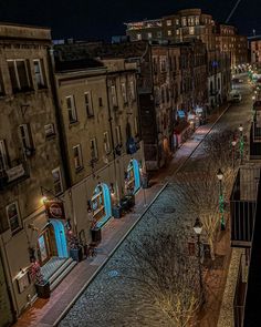 an empty city street at night with lights on the buildings and trees in the foreground