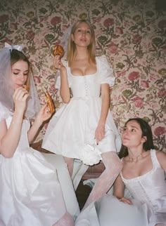 two women in white dresses are eating donuts while another woman sits on the floor