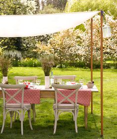 an outdoor dining table set up with pink and white chairs under a canopy in the grass