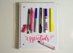 a notebook with pens and writing on the page that says essentials? written in pink ink