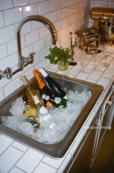 several bottles of alcohol are sitting in the ice cubes on the kitchen sink counter