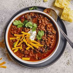 a bowl of chili with cheese and sour cream on the side next to some crackers