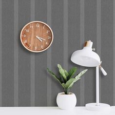 a clock on the wall next to a potted plant in front of a lamp