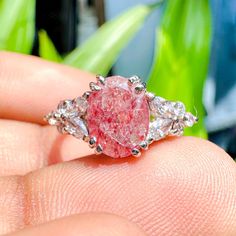 a close up of a person's hand holding a ring with a pink diamond