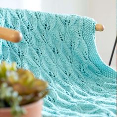 a blue knitted blanket sitting on top of a chair next to a potted plant