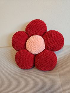 a crocheted red flower sitting on top of a bed next to a white wall