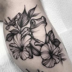 a black and white frog with flowers on his leg, tattoo by the artist in progress