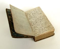 an old book with writing on it sitting on top of a white table next to a cell phone