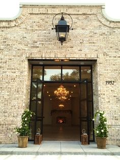 an entrance to a brick building with potted plants on either side and a chandelier hanging from the ceiling