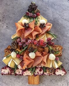 a christmas tree made out of cheese and meats on a wooden stick with pine cones