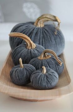 three gray pumpkins are sitting on a wooden platter