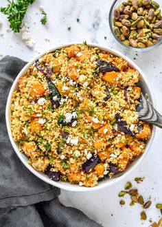 a white bowl filled with carrots, nuts and feta cheese next to a spoon