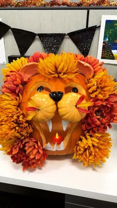 a lion mask with flowers around it's mouth on a white table in front of black and orange flags