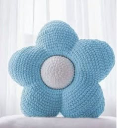 a blue crocheted flower pillow sitting on top of a white bed next to a window