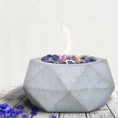 a concrete bowl filled with blue rocks on top of a wooden table next to a lit candle